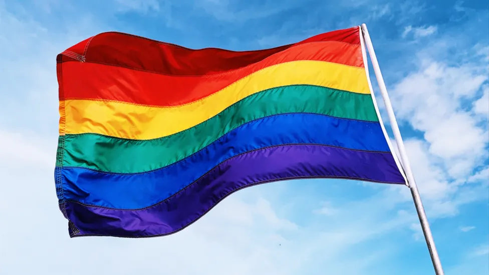 Rainbow flag waving against a blue sky.