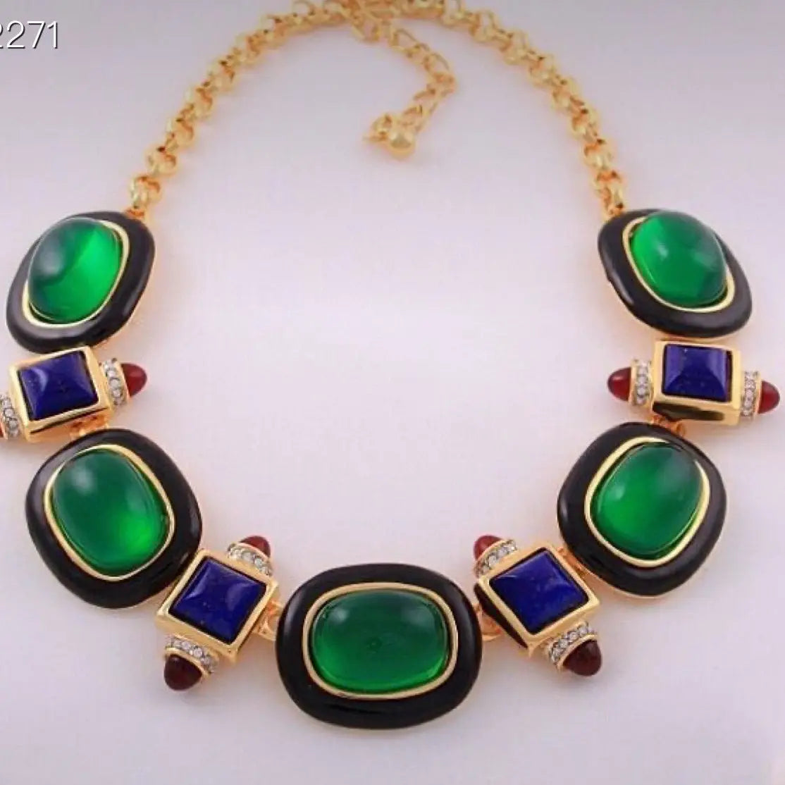 Statement necklace featuring green cabochon stones, blue square gems, and red accents on a gold-toned chain.