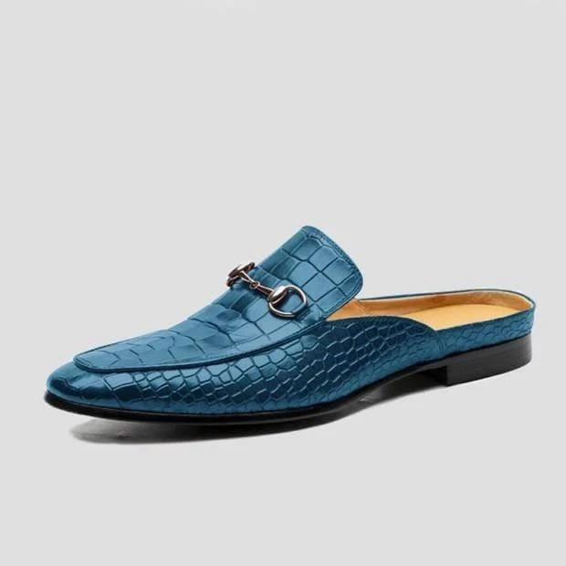 Teal blue crocodile-textured backless moccasin loafers with silver buckle detail.