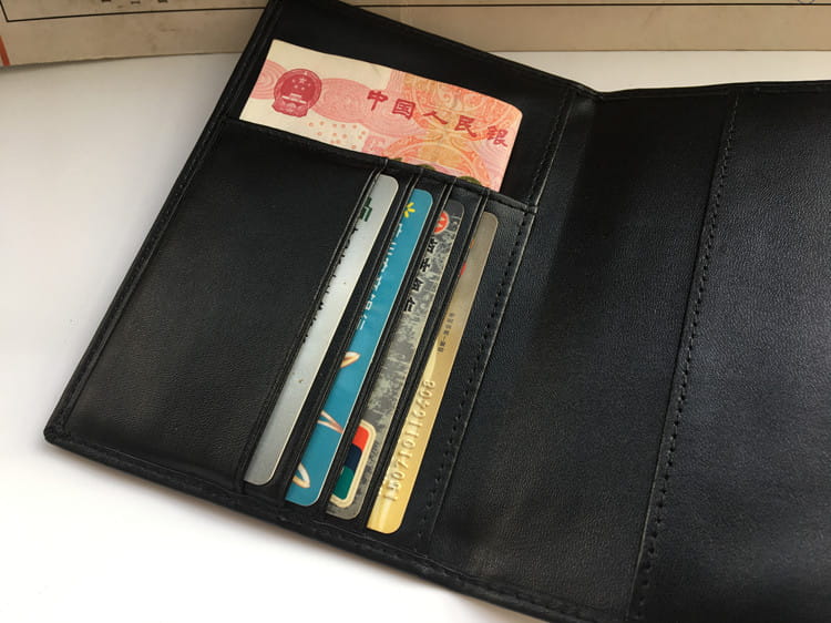 Black leather wallet with RFID protection, holding credit cards and Chinese currency.