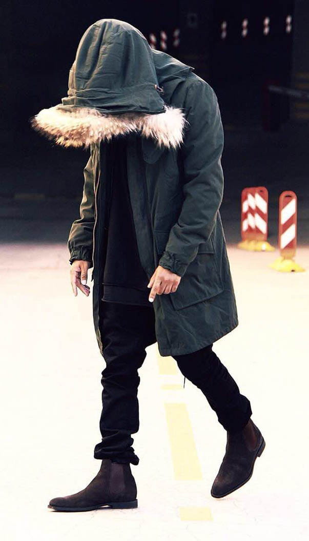 Person in a green parka and black boots showcasing Men’s Suede Pointed Toe High-Top Chelsea Boots.