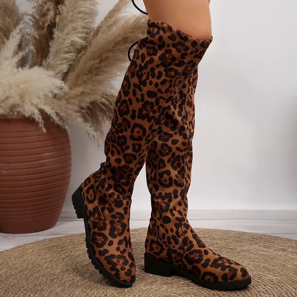 Knee-high leopard print boots with flat sole and lace-up design for trendy style.