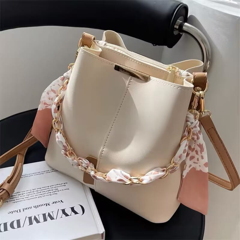 Cream-colored versatile bucket bag with braided strap and brown leather for women’s crossbody fashion.