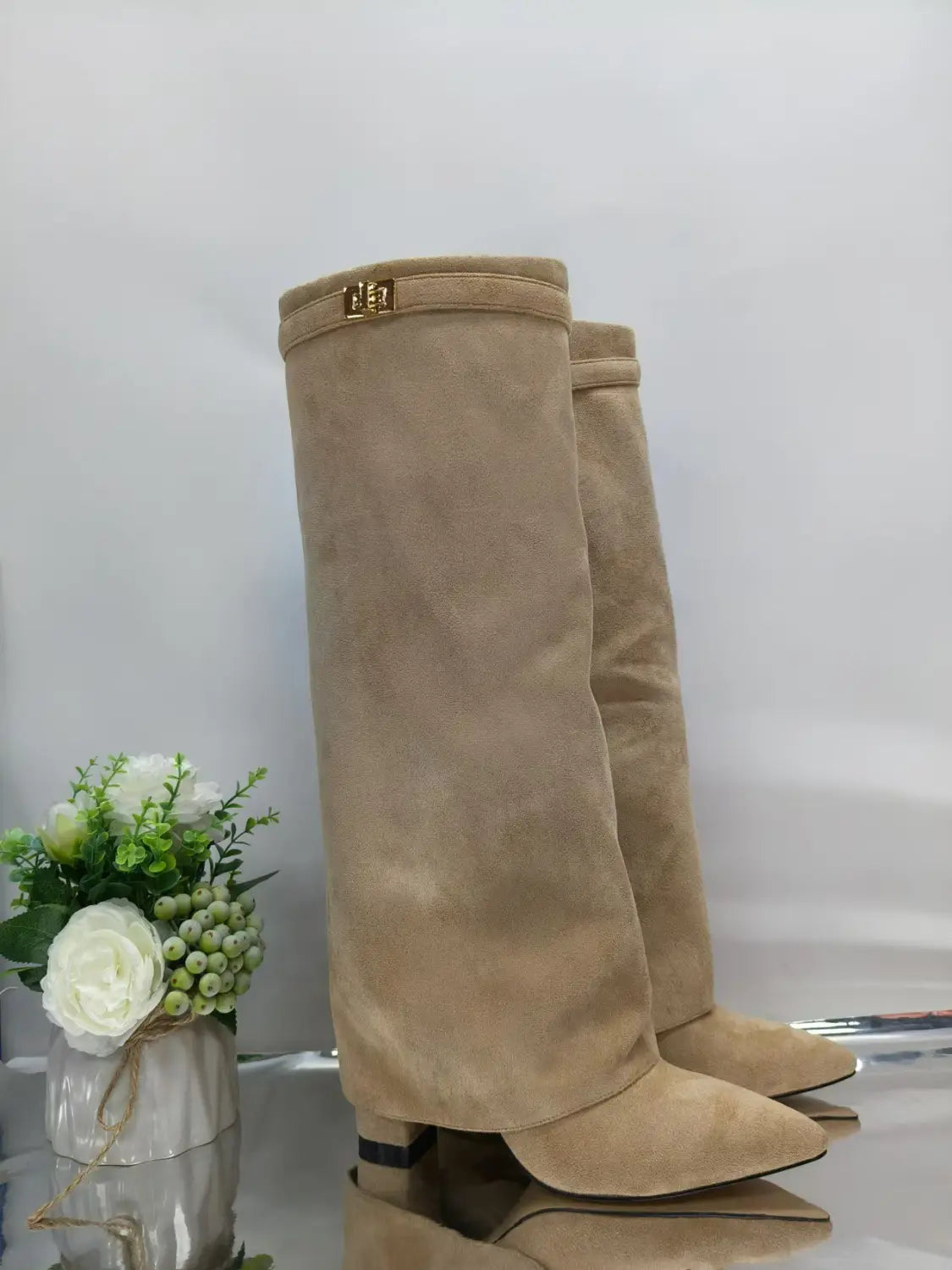 Grandes bottes en daim beige pour femmes, à bout pointu et à boucle métallique au niveau du genou, avec des détails dorés.