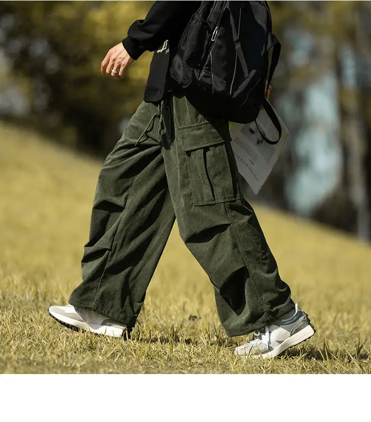 Men’s stylish wide-leg corduroy cargo pants in olive green with pockets and white sneakers.