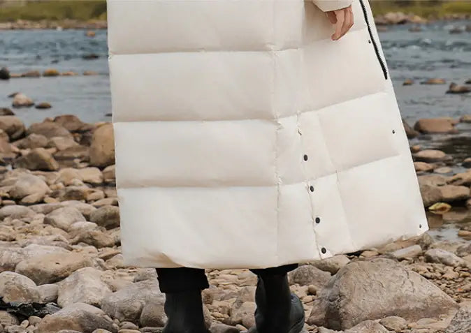 White puffy luxury padded long coat with black buttons styled over black boots.