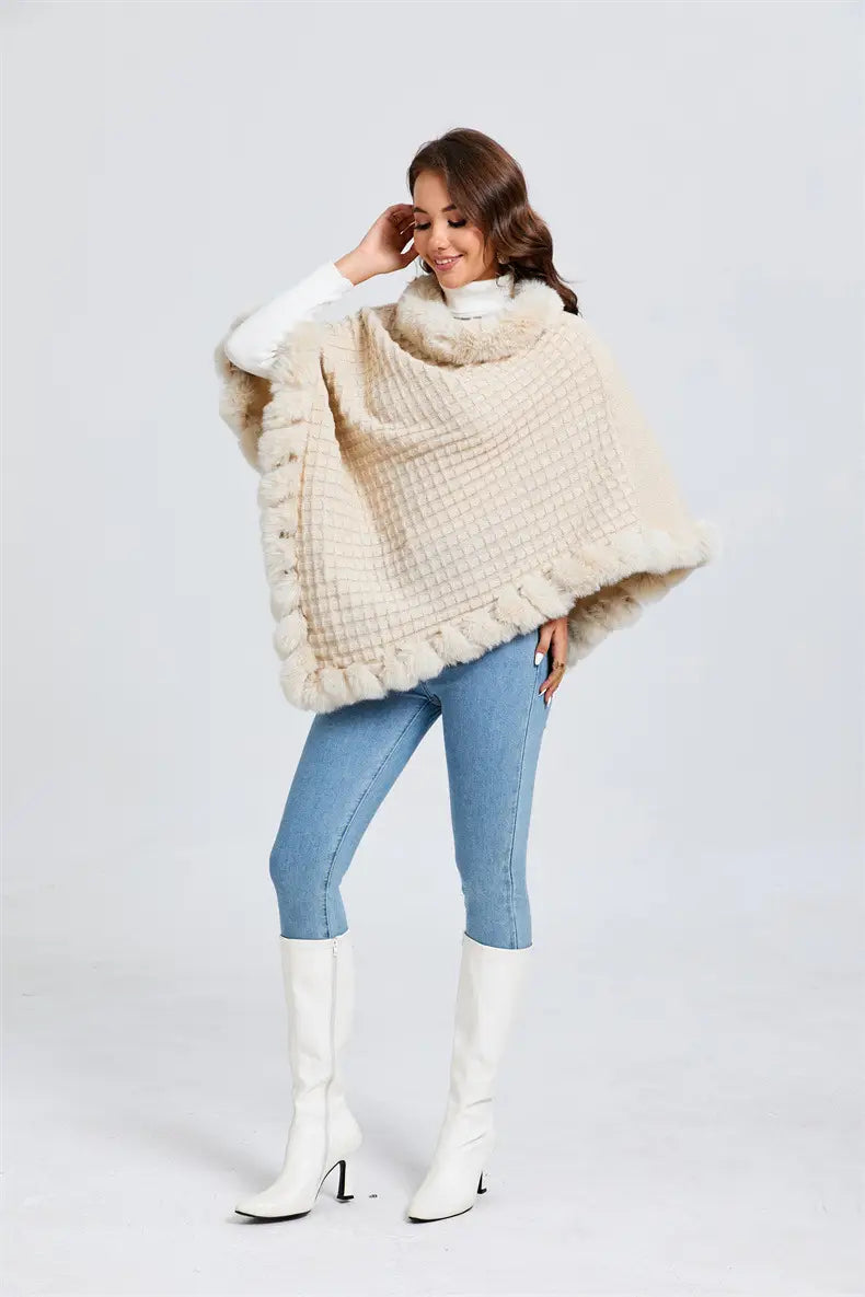 Cream knit poncho with faux fur collar and ruffled edges, styled with jeans and white boots.