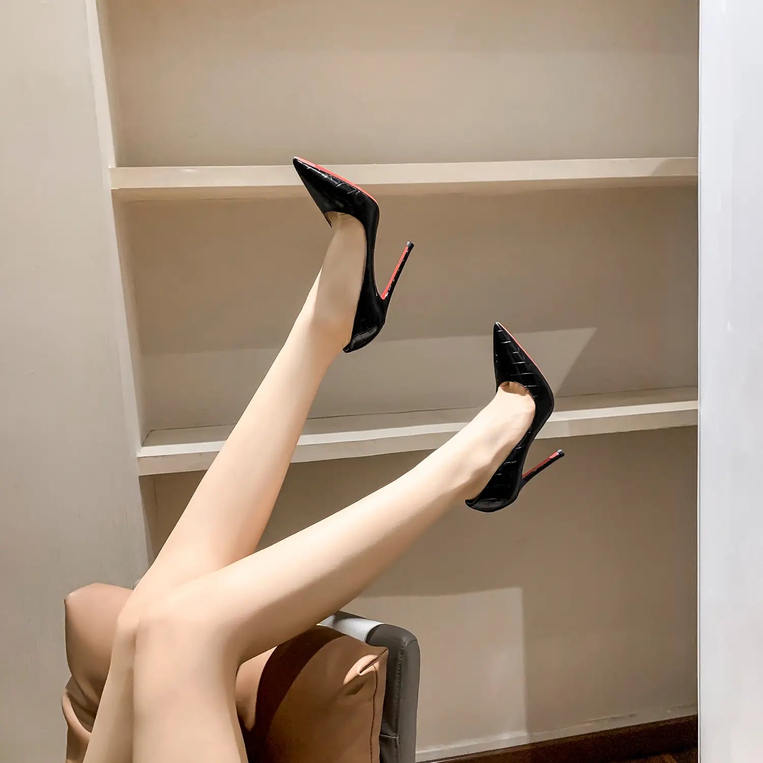 Pair of black patent leather high heels with red soles propped against a wall.