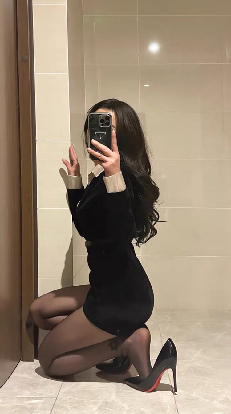 Selfie miroir d'une personne portant une robe noire et des chaussures noires à talons hauts avec des semelles rouges.