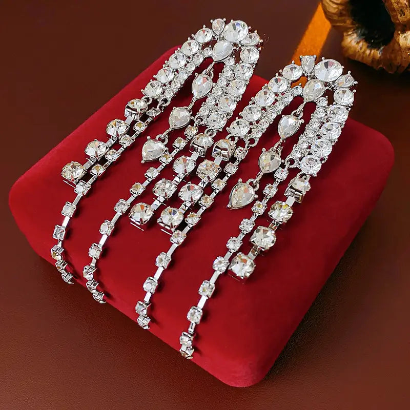 Sparkling rhinestone bracelets on red velvet with water droplet shaped luxury tassel earrings.