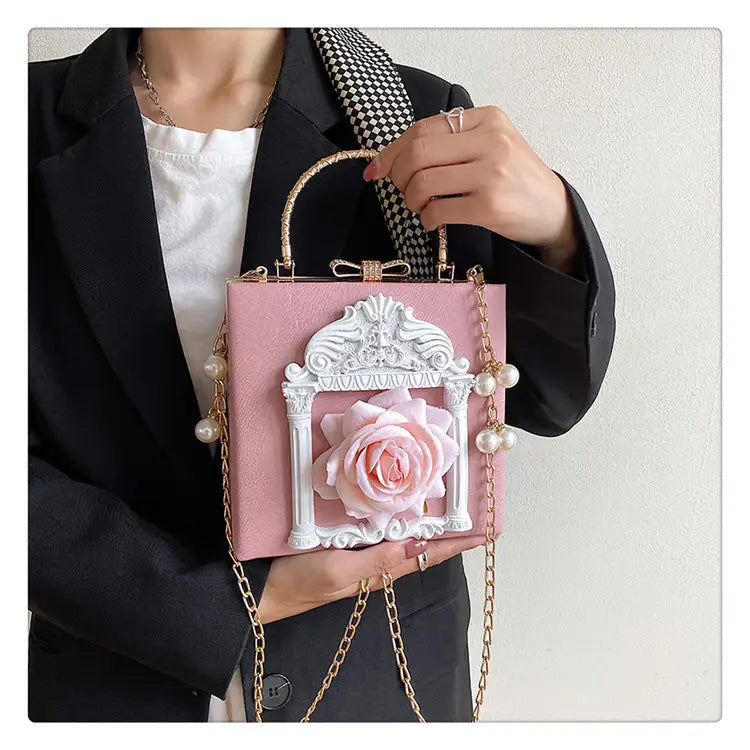 Pink shoulder chain bag with white rose embellishment and pearl strap for a unique touch.