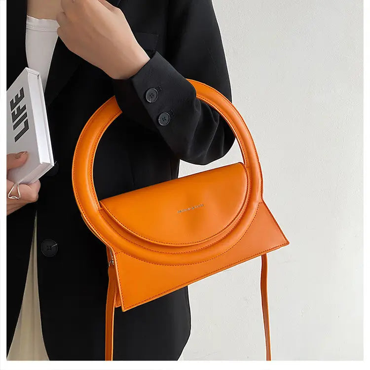 Orange leather handbag with circular handle, a designer handbag versatile for any outfit.