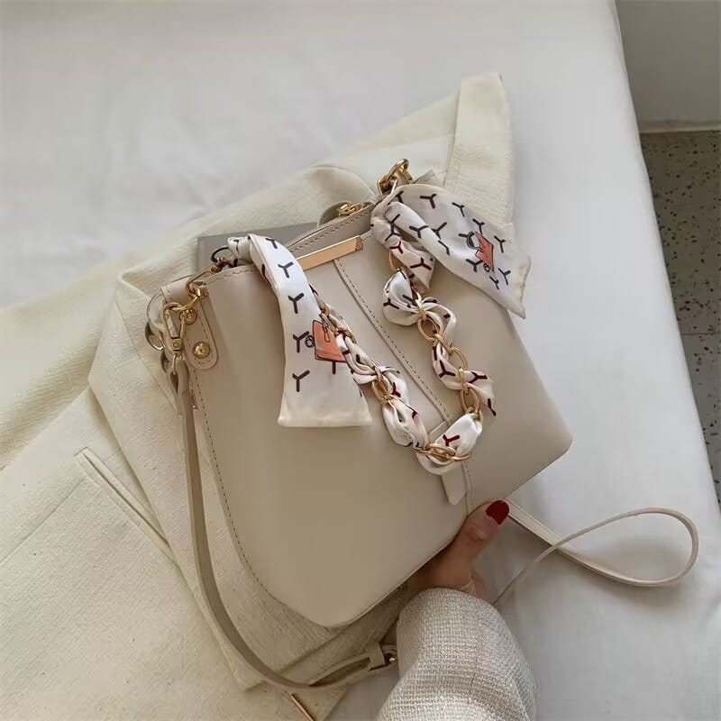 Cream-colored versatile bucket bag with a patterned scarf for women’s crossbody fashion.