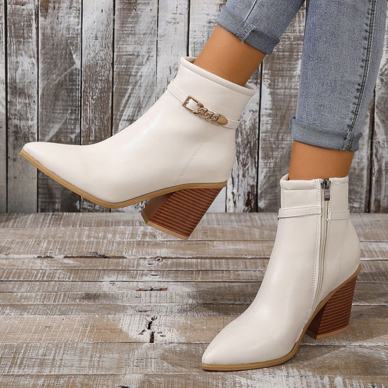 White ankle boots with pointed toes, chunky wooden heels, and gold buckle details.