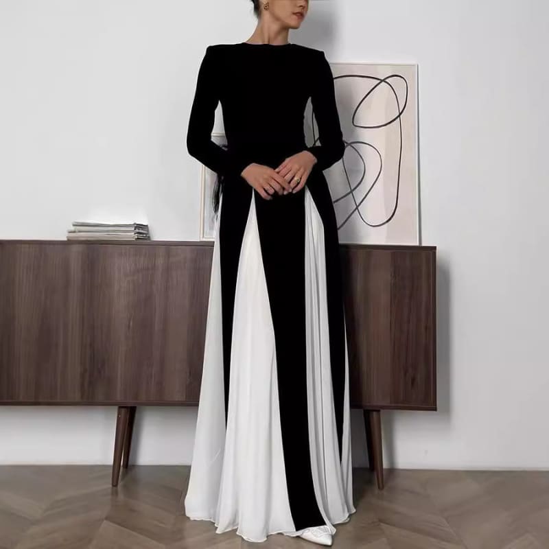 Long-sleeved black and white color-blocked maxi dress with a fitted bodice and flowing skirt.