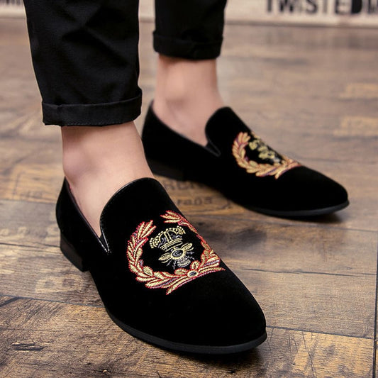 Black velvet loafers with gold embroidered crest designs on the uppers.