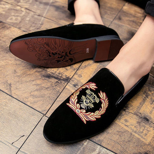 Pair of black velvet loafers with gold embroidered crest design on the upper.