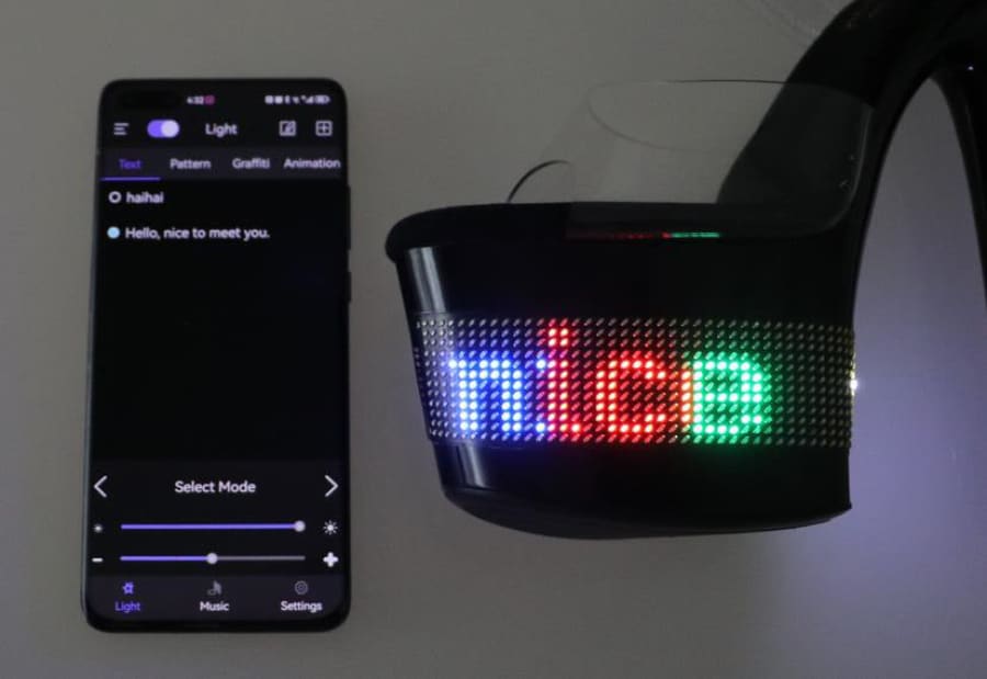 LED display mask with colorful text alongside a smartphone showing a control interface.