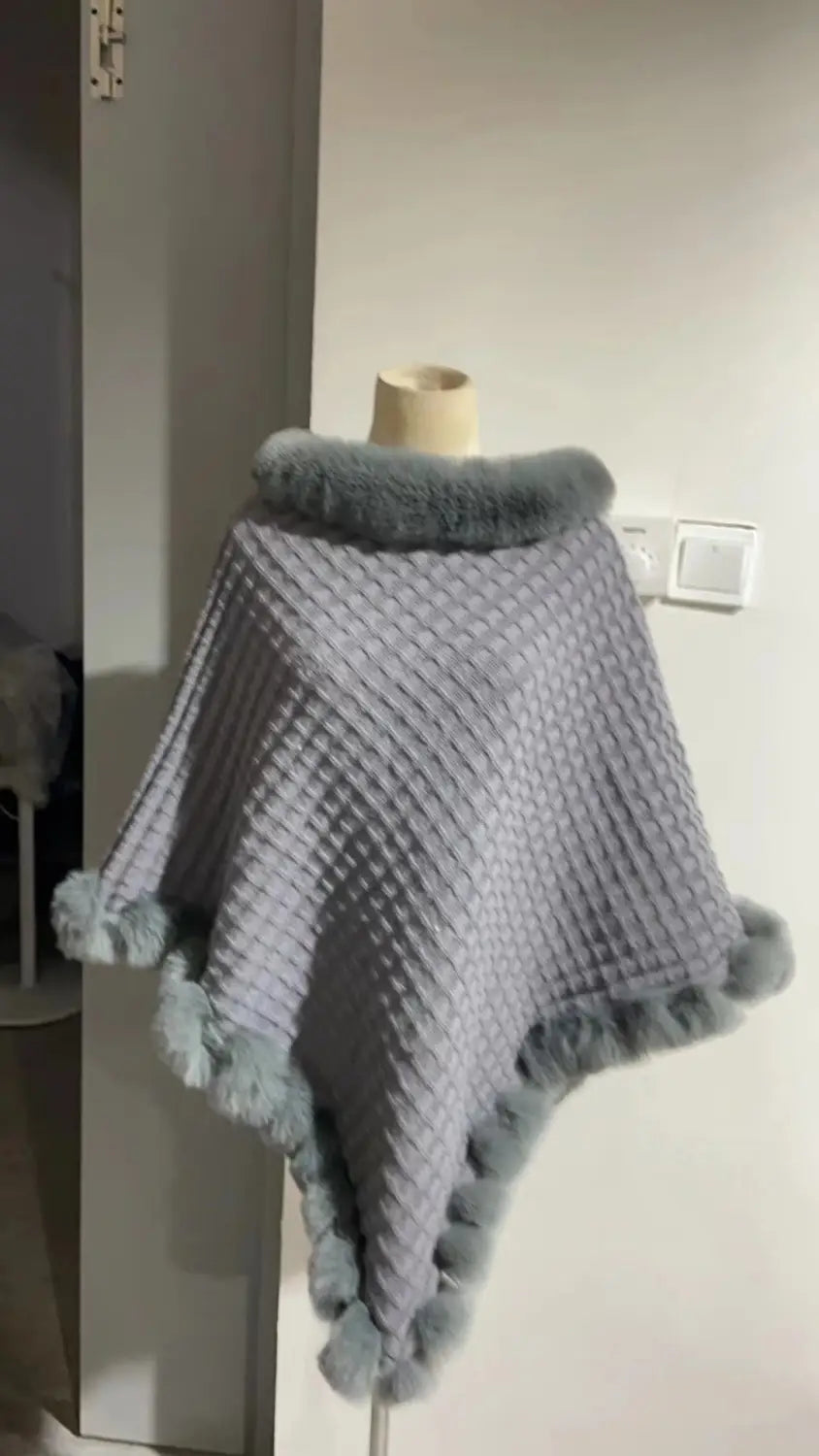 Gray knitted poncho with faux fur collar and pom-pom details for cozy style.