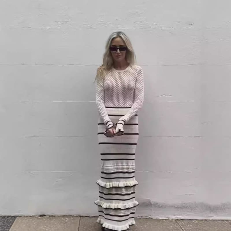 Woman wearing a long striped skirt and white knit top.