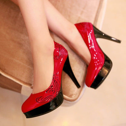 Pair of glossy red high-heeled shoes with black platforms and decorative swirl patterns.