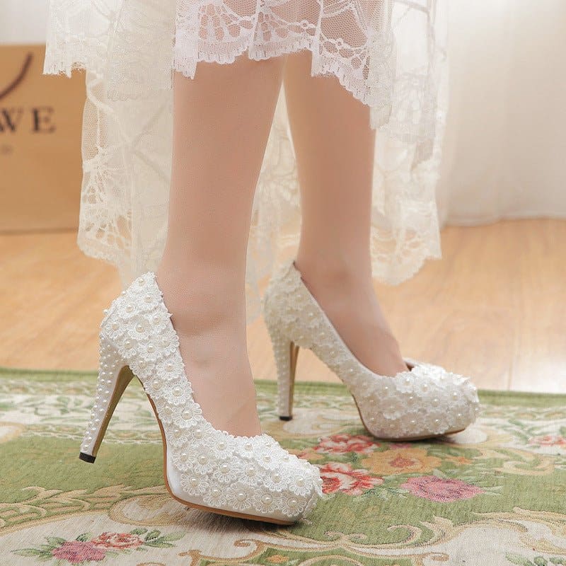 White lace high-heeled wedding shoes with floral embellishments.