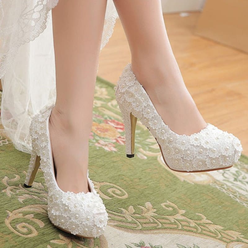 Elegant white lace high-heeled bridal shoes with floral embellishments.