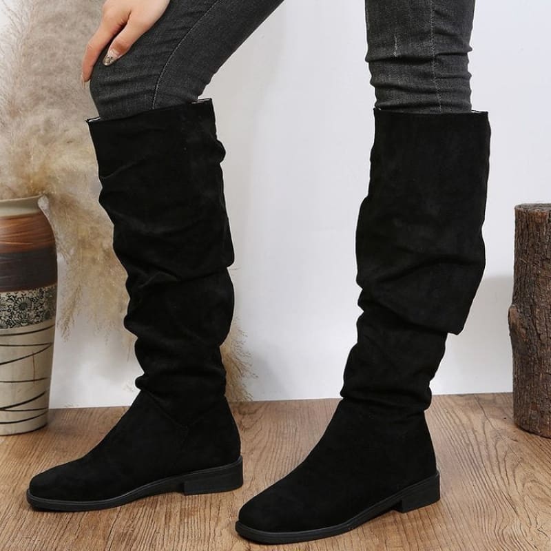 Pair of tall black suede slouchy boots with flat soles.