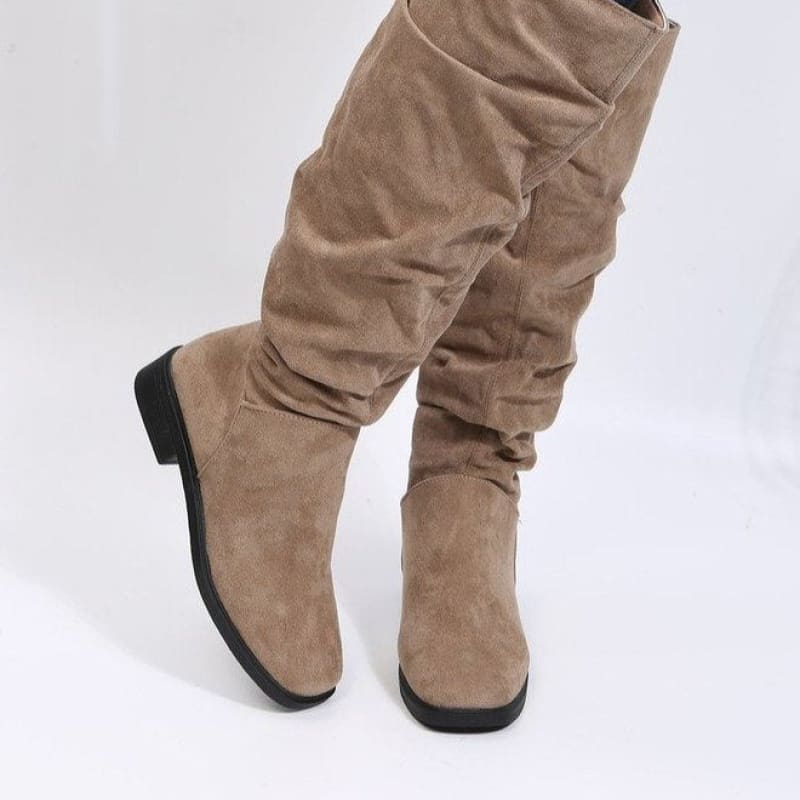 Pair of tall, slouchy beige suede boots with flat soles.