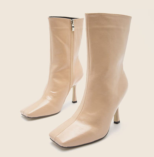 Pair of beige high-heeled ankle boots with square toes and side zippers.