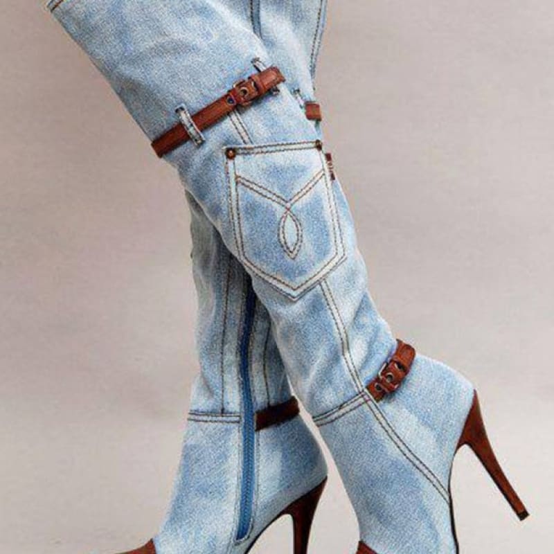 Knee-high denim stiletto boots with brown leather straps and accents.