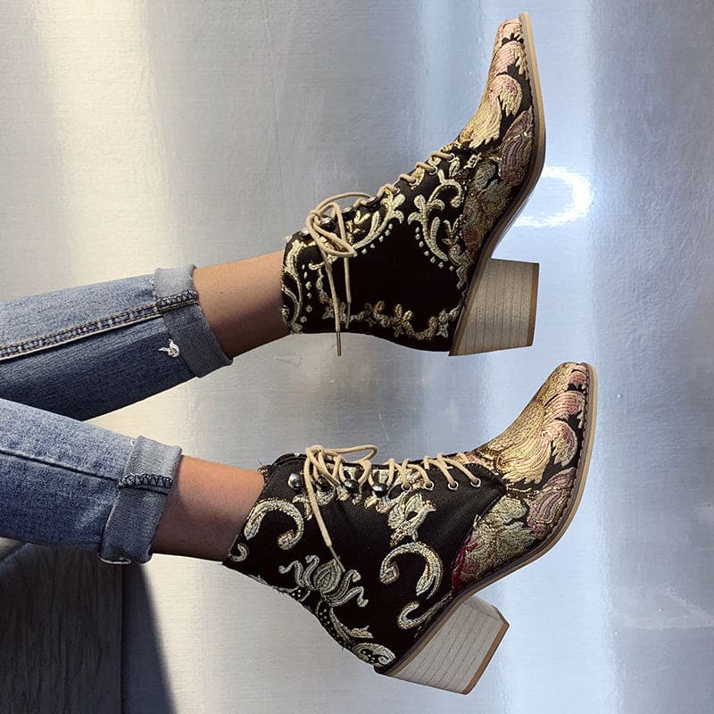 Ornate ankle boots with embroidered floral patterns on a dark background and chunky wooden heels.