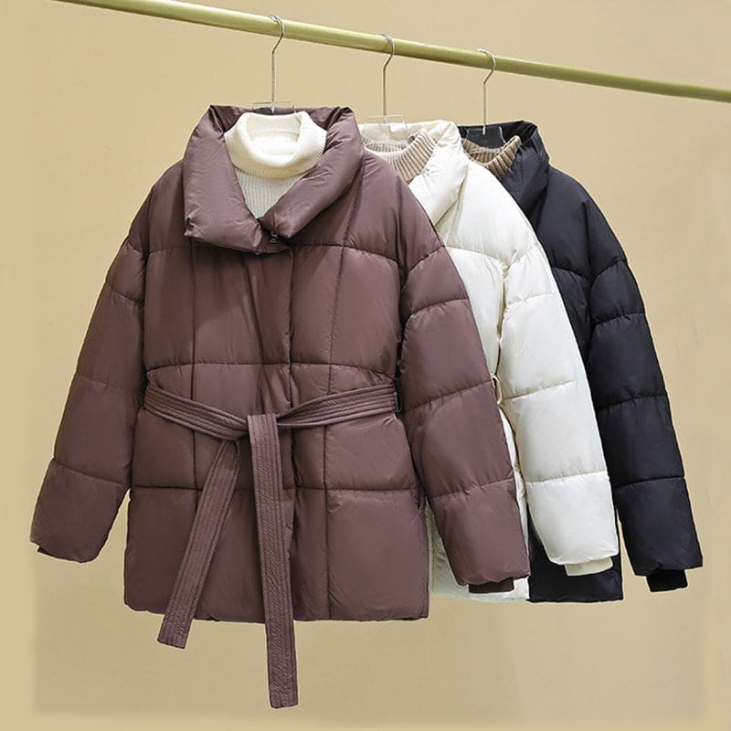 Puffy winter coats in brown, white, and black hanging on a rod.