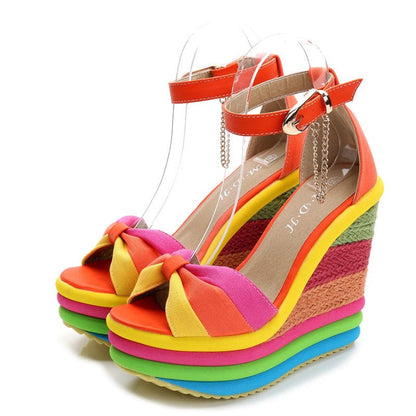 Colorful rainbow-striped platform wedge sandals with ankle straps and a bow detail.