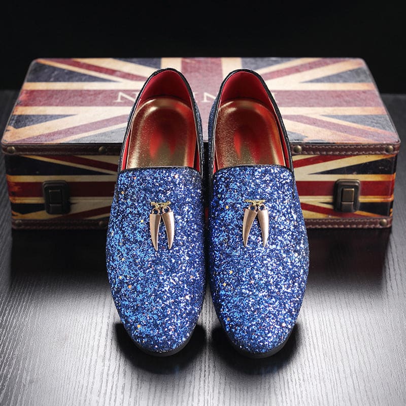 Pair of blue glittery loafers with metallic tooth-shaped ornaments on top.