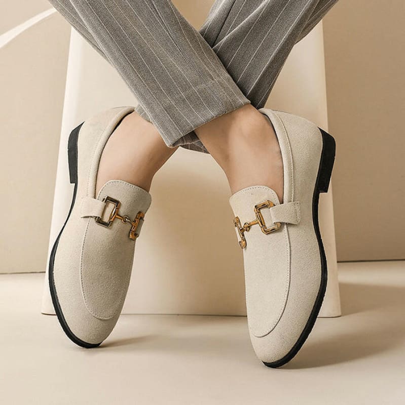 Pair of cream-colored loafers with gold buckle details and black soles.