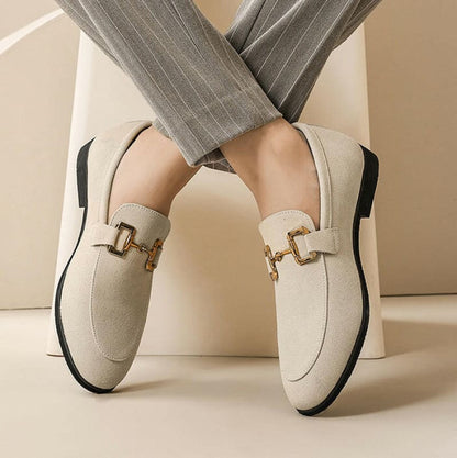 Pair of cream-colored loafers with gold buckle details and black soles.