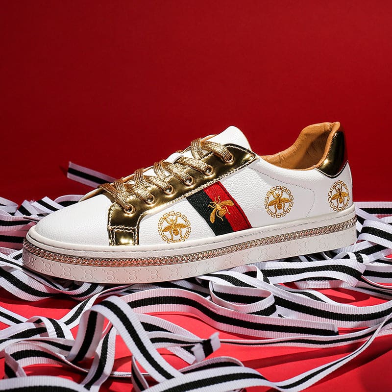 Designer sneaker with white, gold, and red accents featuring bee emblems.