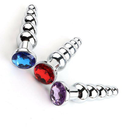 Metal anal plugs with colored jewel-like ends in blue, red, and purple.