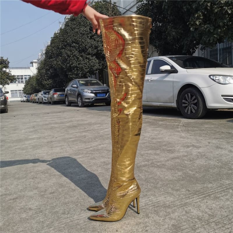 Gold metallic thigh-high stiletto boot with pointed toe and embroidered design.