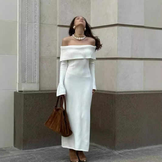 Woman wearing a long white off-shoulder dress and holding a brown handbag.