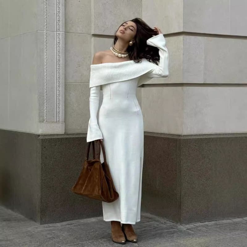 Woman wearing a long white off-shoulder dress and holding a brown handbag.