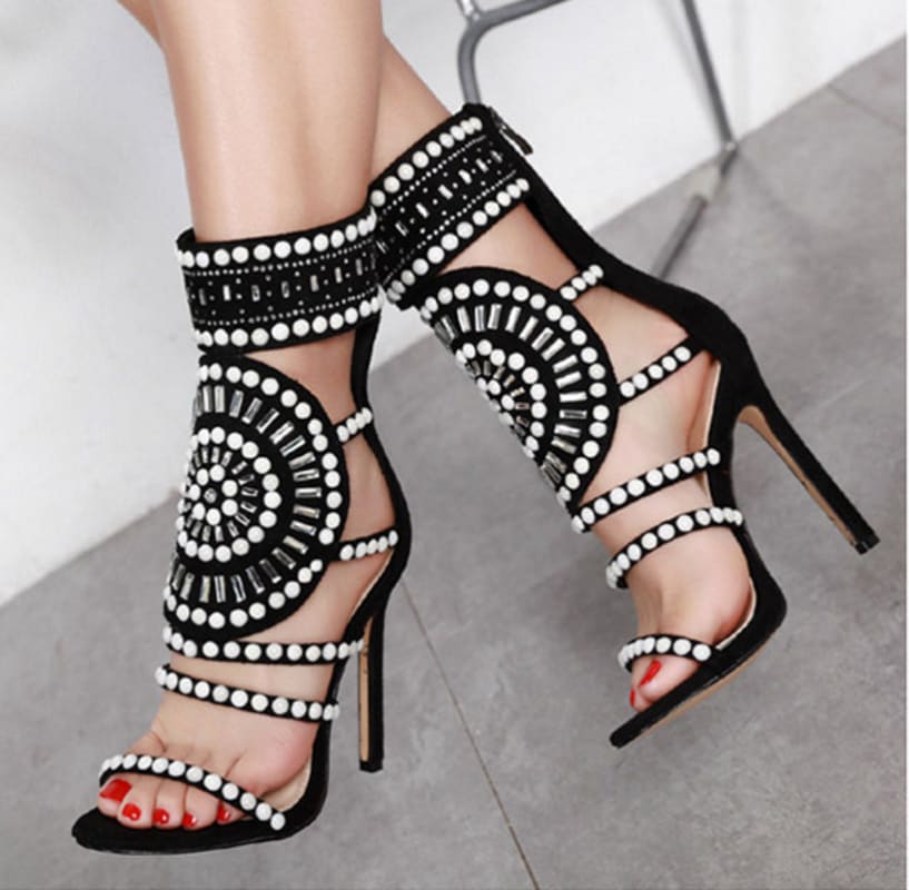 Ornate black high-heeled sandals adorned with intricate white beaded patterns and straps.