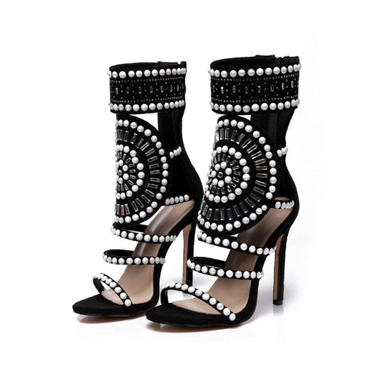 Pair of black high-heeled sandals adorned with white beads in intricate patterns.