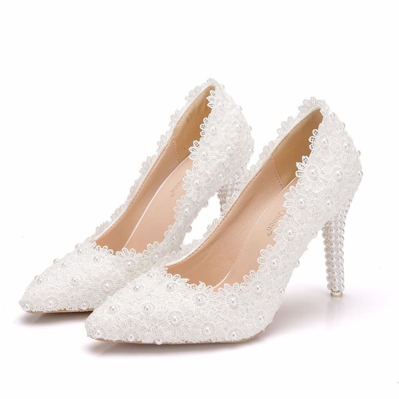 Pair of white lace high-heeled bridal shoes adorned with pearls and floral embellishments.