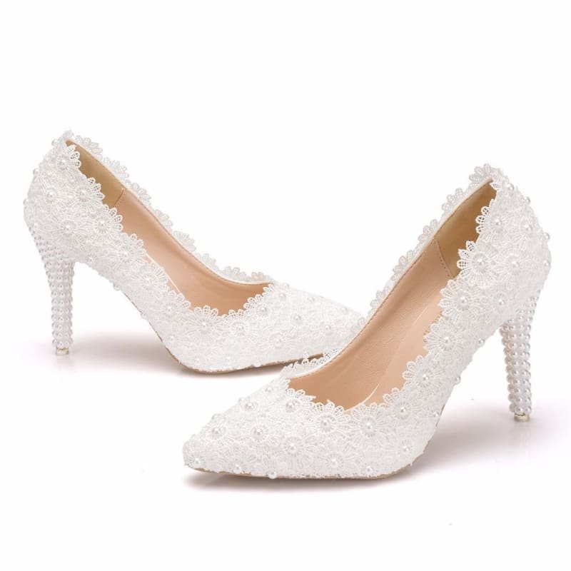 Pair of white high-heeled shoes adorned with lace and pearls.