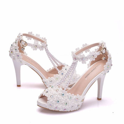 Ornate white high-heeled sandals adorned with pearls and crystals.