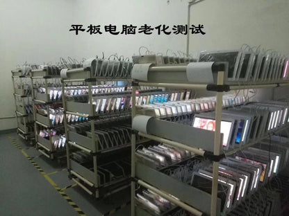 Rows of tablet computers or screens on metal racks undergoing testing or quality control.