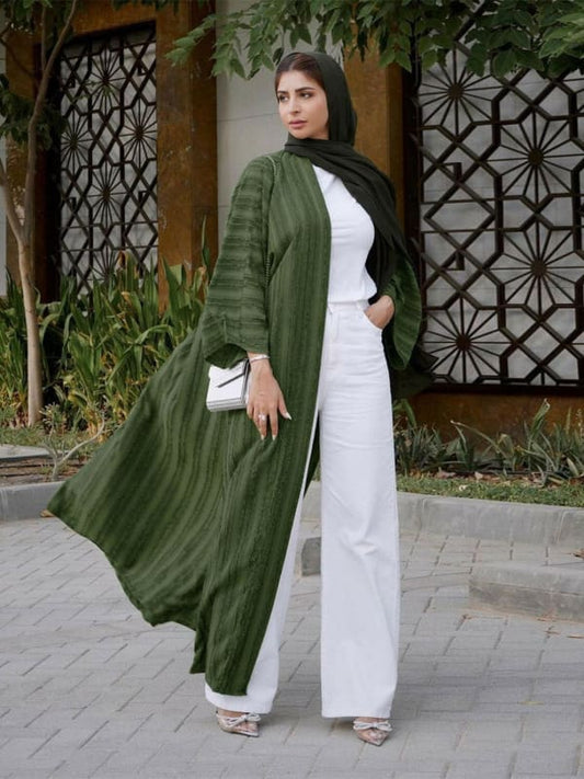 Long green open coat worn over a white outfit with a black headscarf.