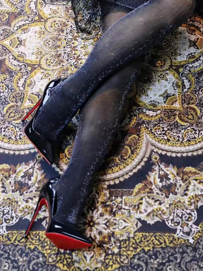 Pair of black high-heeled shoes with red soles worn on feet resting on an ornate patterned rug.